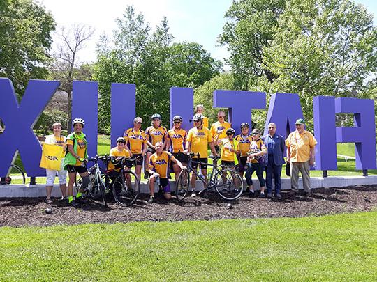group of bicyclists in front of Fiat Lux sign on Alfred University campus
